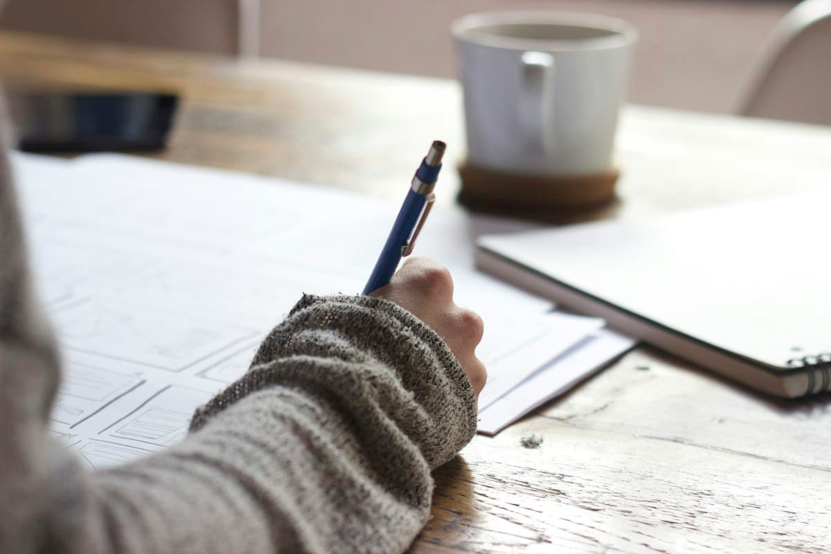 A hand writing notes in a notebook beside a coffee cup in warm light